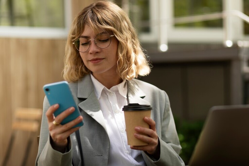 Mulher olhando celular com café na mão